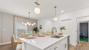 Une cuisine moderne dotée d’un îlot central, de meubles blancs et d’un éclairage suspendu.