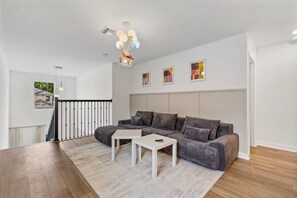 Ein modernes Wohnzimmer mit einem Ecksofa, zwei weißen Beistelltischen, einer Pendelleuchte und Blick ins Freie.