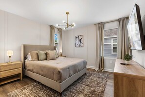 Ein Schlafzimmer mit Bett, Nachttisch, Lampe und einem Fernseher auf einem Holzständer.