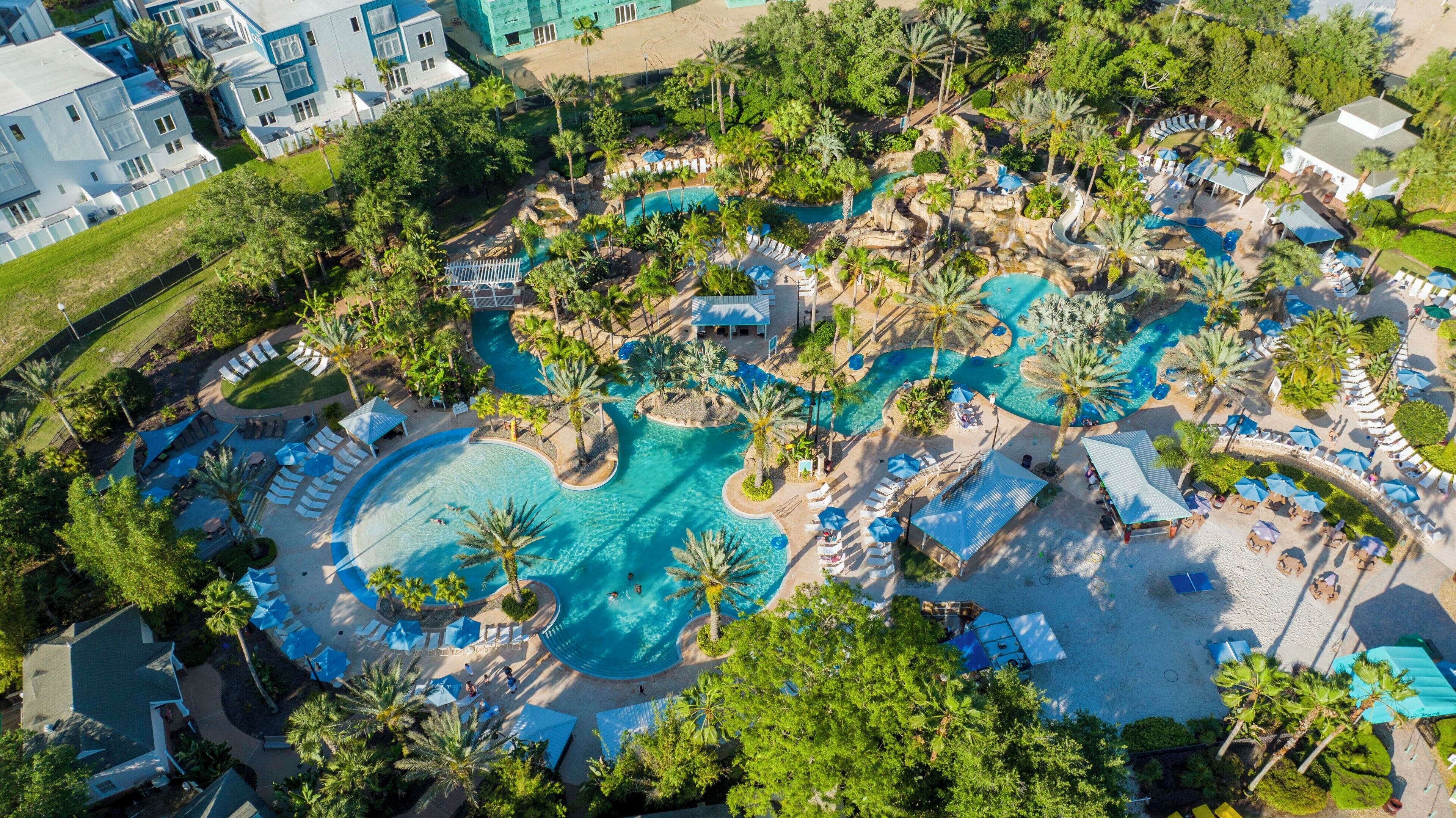 An aerial view of a resort with multiple swimming pools, palm trees, and lounge areas.