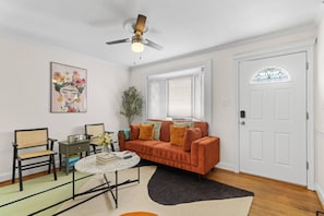 Una sala de estar con sofá, mesa de centro, sillón, lámpara de pie, un cuadro y una puerta con ventana.