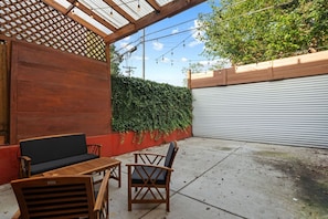 Un patio al aire libre con mobiliario de madera, un muro rojo y una pared cubierta de hiedra verde.