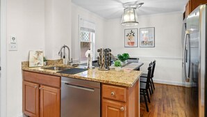 A kitchen with a granite countertop, stainless steel appliances, wooden cabinets, and a dining area with a table and chairs. - Family-Friendly 3BR Home Near DC (Arlington)