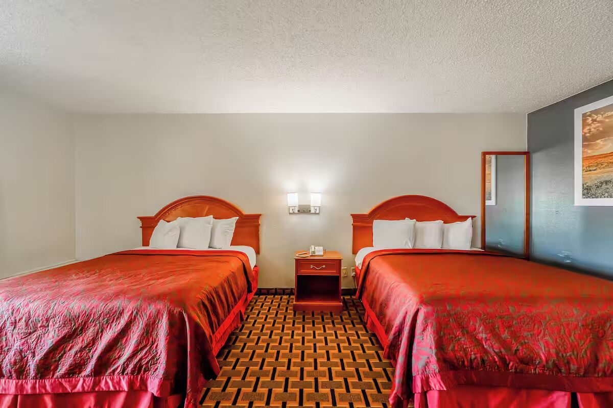 A hotel room with two beds, a nightstand, and a wall-mounted light fixture.