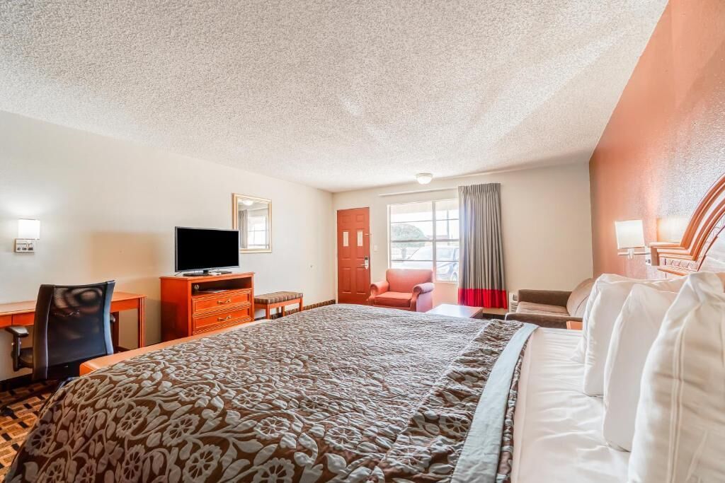Una habitación de hotel con una cama grande, un escritorio, un televisor y una ventana con cortinas.