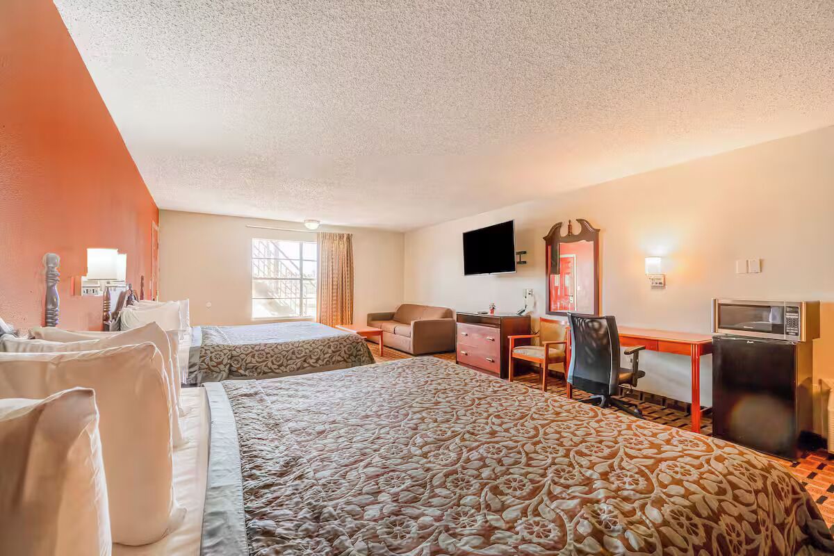 Une chambre d’hôtel avec deux lits, un bureau, une chaise, une télévision et un four à micro-ondes.
