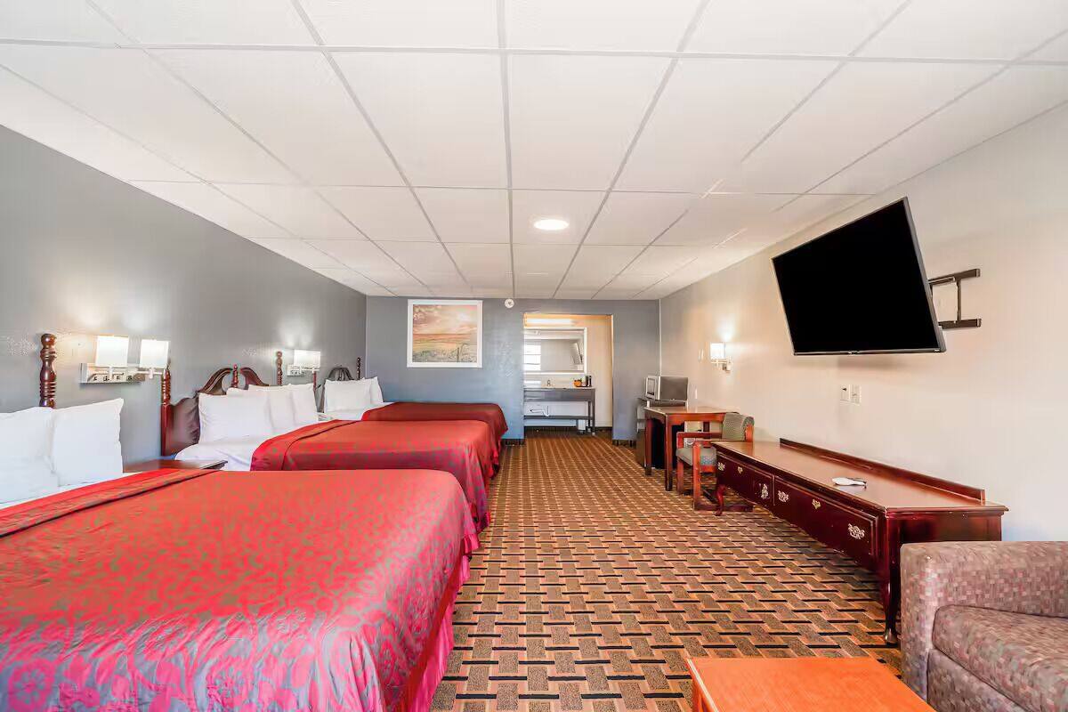 A hotel room with three beds, a television, a desk, and a patterned carpet.
