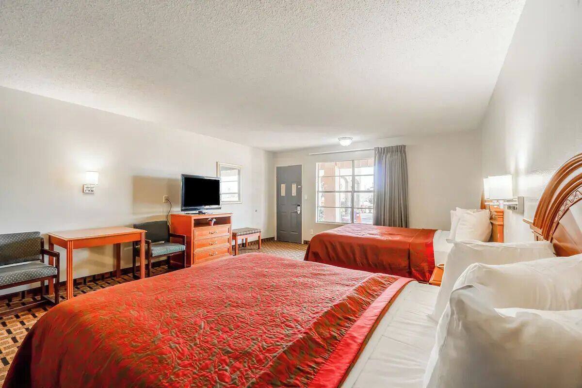 A hotel room with two beds, a desk with a TV, a chair, a dresser, and a window with curtains.