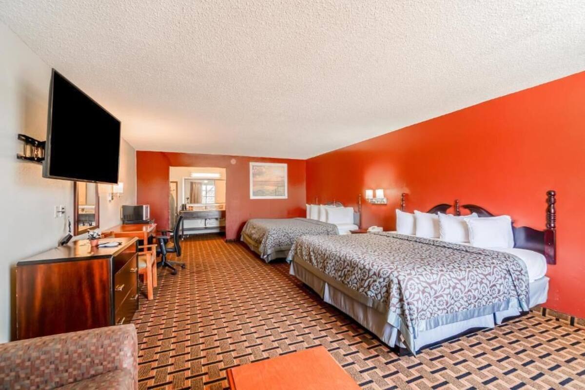 A hotel room with two beds, a desk with a TV, a chair, and a patterned carpet.