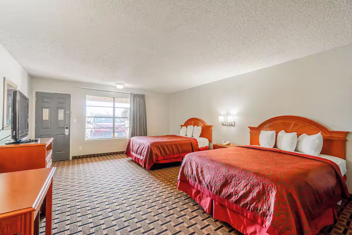 Een hotelkamer met twee bedden, een bureau, een televisie en een raam met gordijnen.