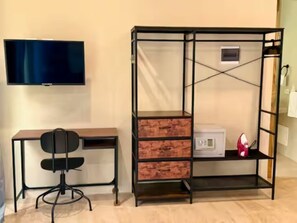 Una habitación con escritorio, silla, televisión y una estantería metálica con cajones.