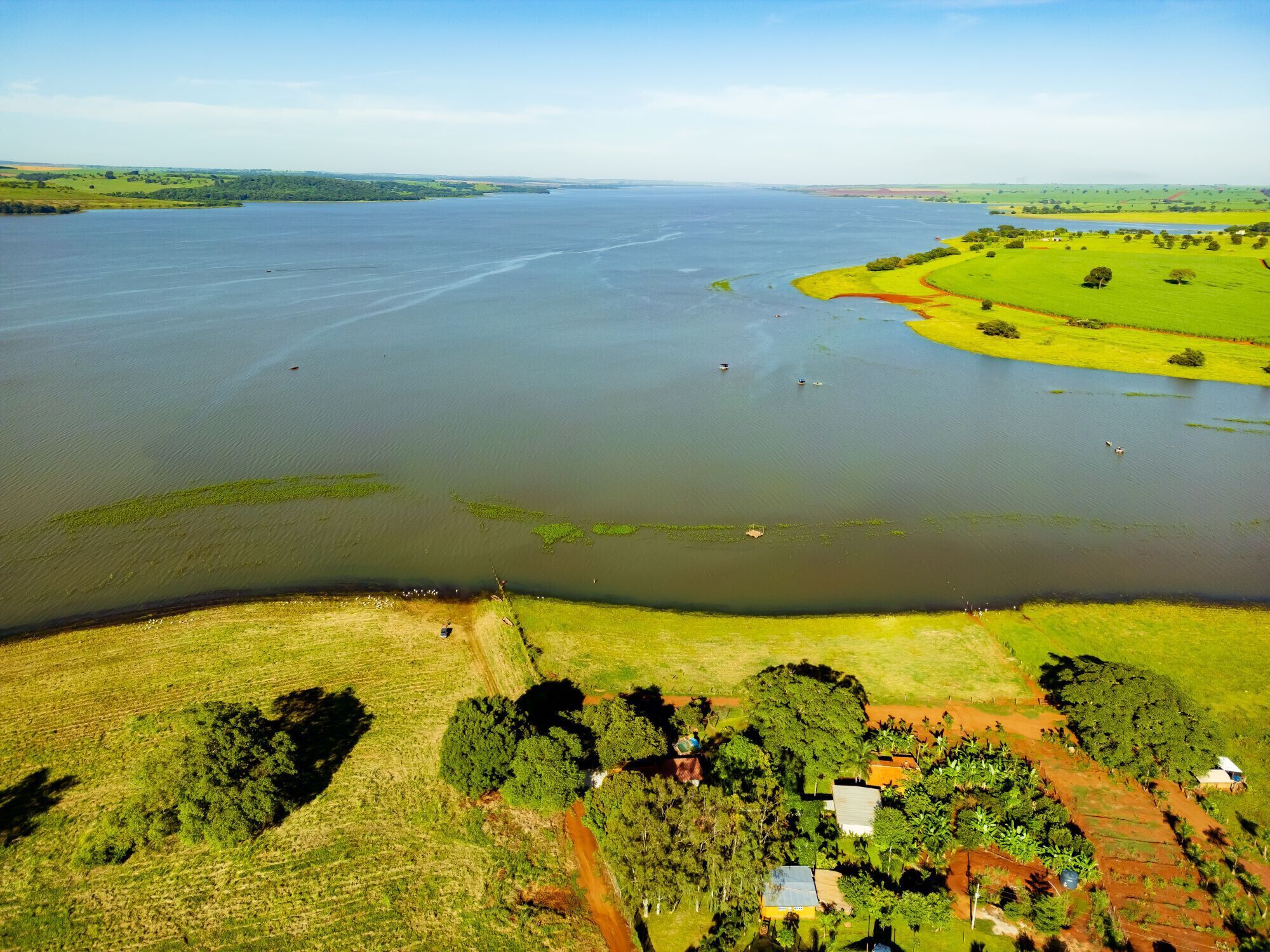 An aerial view of a coastal area with a large body of water, green fields, and scattered buildings.