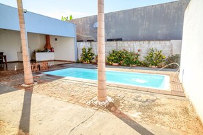 A swimming pool with two separate sections, surrounded by a patio area with a brick floor and a concrete wall. - Casa c Piscina Churrasqueira Perto do Rio Grande (Itapagipe)