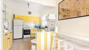 A kitchen with yellow cabinets, a white refrigerator, a stove, and a microwave. There is a clock on the wall and a newspaper on the wall. - Beauts - Pet Friendly - 5 Mins Walk to Beach (Culburra Beach)