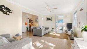 A modern living room with a grey sofa, a coffee table, a TV, and a bookshelf. - Beauts - Pet Friendly - 5 Mins Walk to Beach (Culburra Beach)