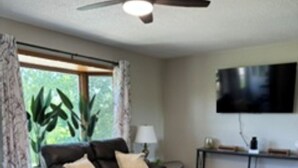 Una sala de estar con un sofá, una mesa de centro, un televisor montado en la pared y un ventilador de techo.