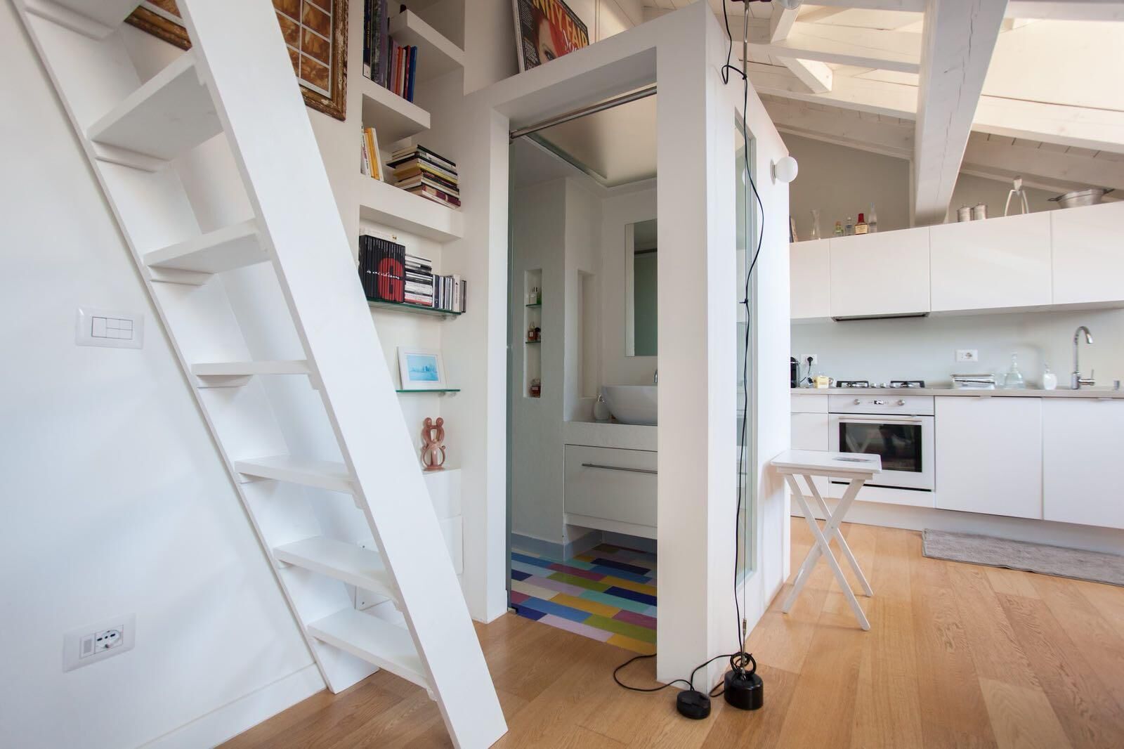 Een moderne keuken met witte kastjes, een ingebouwde oven en een kleine eethoek met een tafel en stoelen.