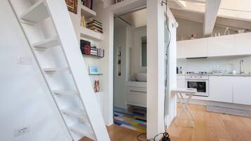 Een moderne keuken met witte kastjes, een ingebouwde oven en een kleine eethoek met een tafel en stoelen.