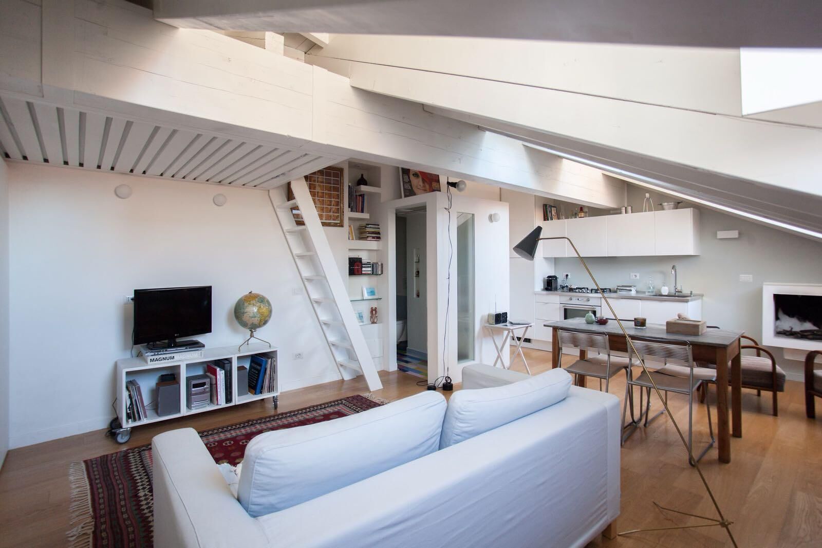Een modern loft appartement met een witte bank, een eethoek, een keuken en een trap.