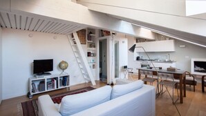 Un loft moderno con sofá blanco, comedor, cocina y una escalera.