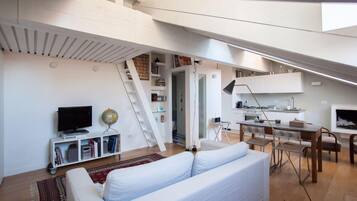 Een modern loft appartement met een witte bank, een eethoek, een keuken en een trap.