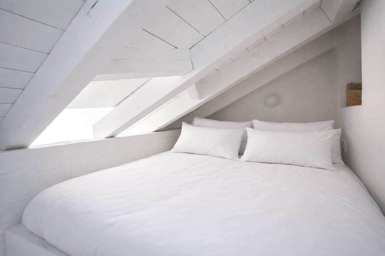 Een slaapkamer met een schuine kap en dakraam, met een groot bed met witte beddengoed.