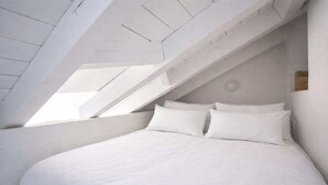 Un dormitorio con techo inclinado y tragaluces, que cuenta con una cama grande con ropa de cama blanca.
