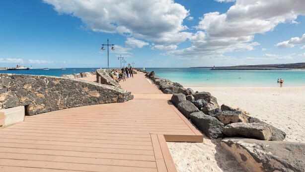 A wooden boardwalk leading to a sandy beach with a clear blue sky and calm sea. - Home2Book Elegant City Escape with Terrace (Puerto Lajas)