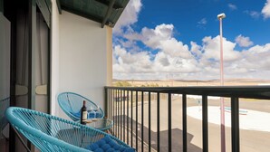 A balcony with two blue chairs, a small table with a bottle, and a view of a parking lot and distant hills under a partly cloudy sky. - Home2Book Elegant City Escape with Terrace (Puerto Lajas)