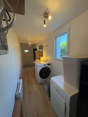 A laundry room with a washing machine, dryer, and a window with a view of greenery outside. - Villa Tregana Beach: comfort and immersion in an idyllic landscape (Locmaria-Plouzané)