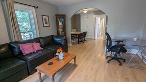 A living room with a leather sofa, a wooden coffee table, and a glass dining table with chairs. There is a door leading to another room and a window with curtains. - Upper 2-bedroom apartment near down-town Chippewa Falls (Chippewa Falls)