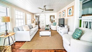 A spacious living room with a white sofa, a coffee table, and a TV. There are framed pictures on the wall and a ceiling fan. - 466 Marlin Dr. - Nice 2 Bedroom with Beach Chair Service Included! (Panama City Beach)