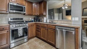 A kitchen with wooden cabinets, stainless steel appliances, a dishwasher, and a tiled backsplash. - 3-bedroom house in Coweta close to Broken Arrow (Coweta)