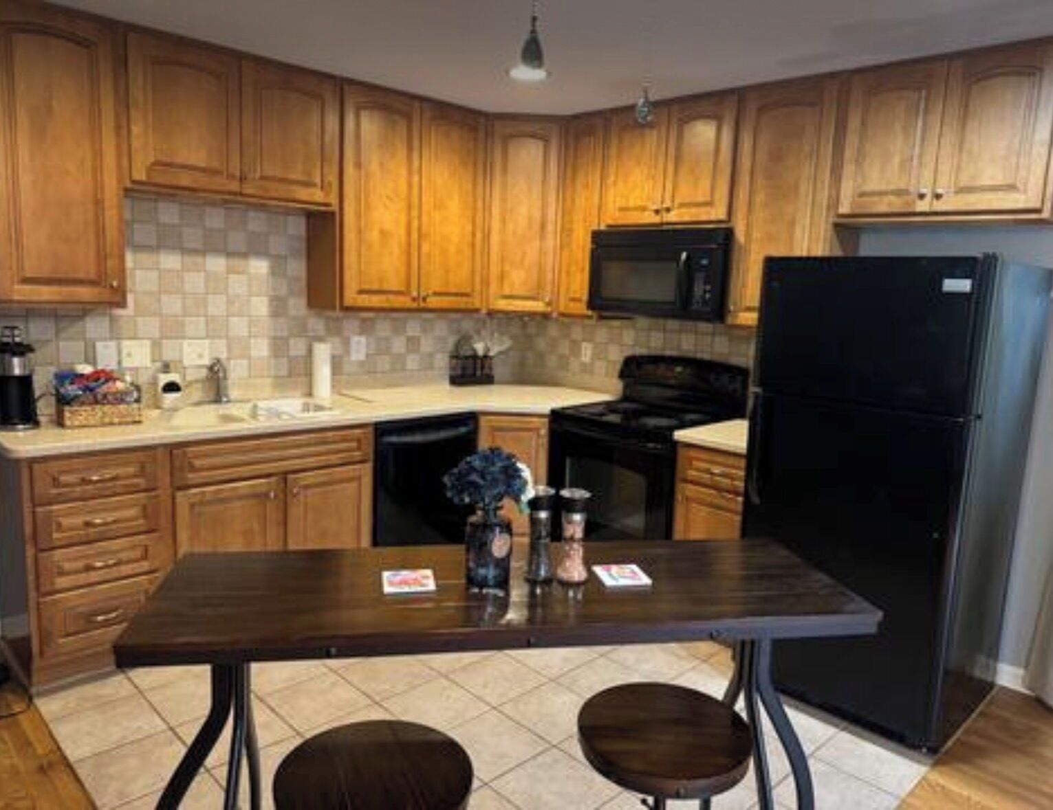 A kitchen with wooden cabinets, a black refrigerator, a microwave, and a dining table with two chairs.