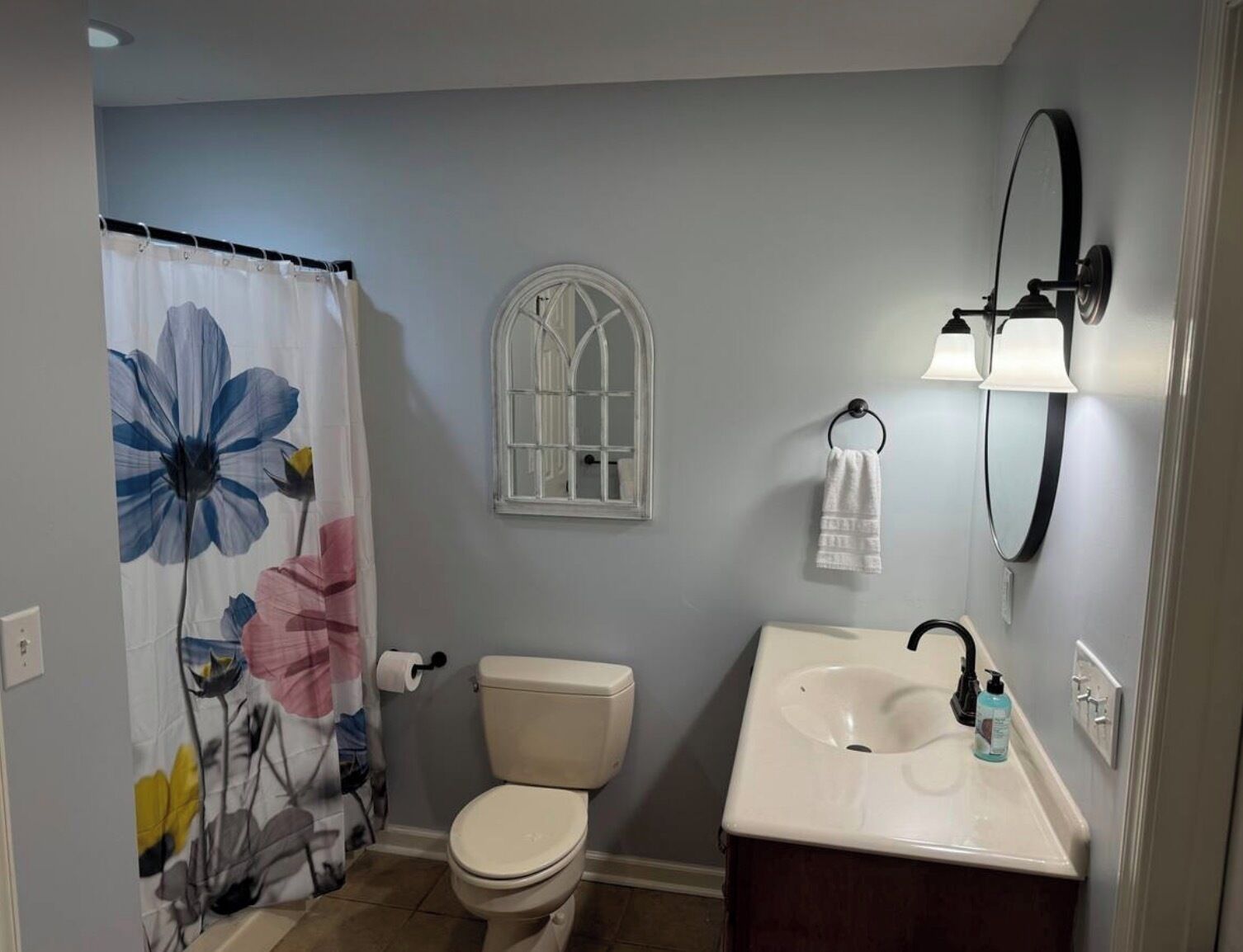 A bathroom with a toilet, sink, shower curtain, window, towel rack, and a mirror.