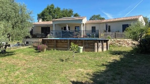 Una casa de dos pisos con piscina, rodeada por una cerca de madera y árboles.