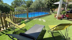 Un patio trasero con piscina, dos sillones de descanso y una valla de madera.