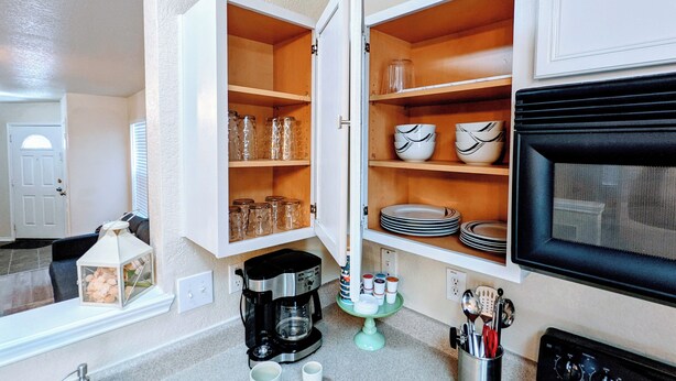 A kitchen with open cabinets containing glassware and plates, a coffee maker, and a microwave. - Cozy 2-bedroom home, North East San Antonio (San Antonio)