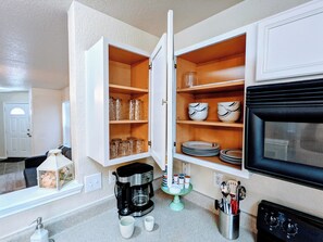 A kitchen with open cabinets containing glassware and plates, a coffee maker, and a microwave. - Cozy 2-bedroom home, North East San Antonio (San Antonio)