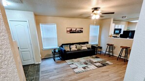 A living room with a sofa, a coffee table, and a rug. There is a ceiling fan and a kitchen area with a microwave. - Cozy 2-bedroom home, North East San Antonio (San Antonio)