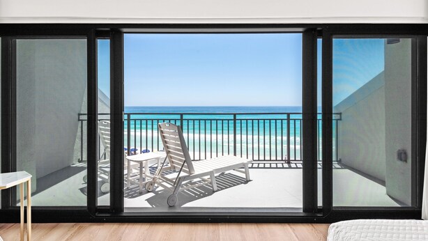 En balkon med udsigt over stranden, en stol og et bord.