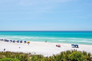 Une plage de sable blanc, avec une eau d’un bleu limpide et plusieurs parasols.