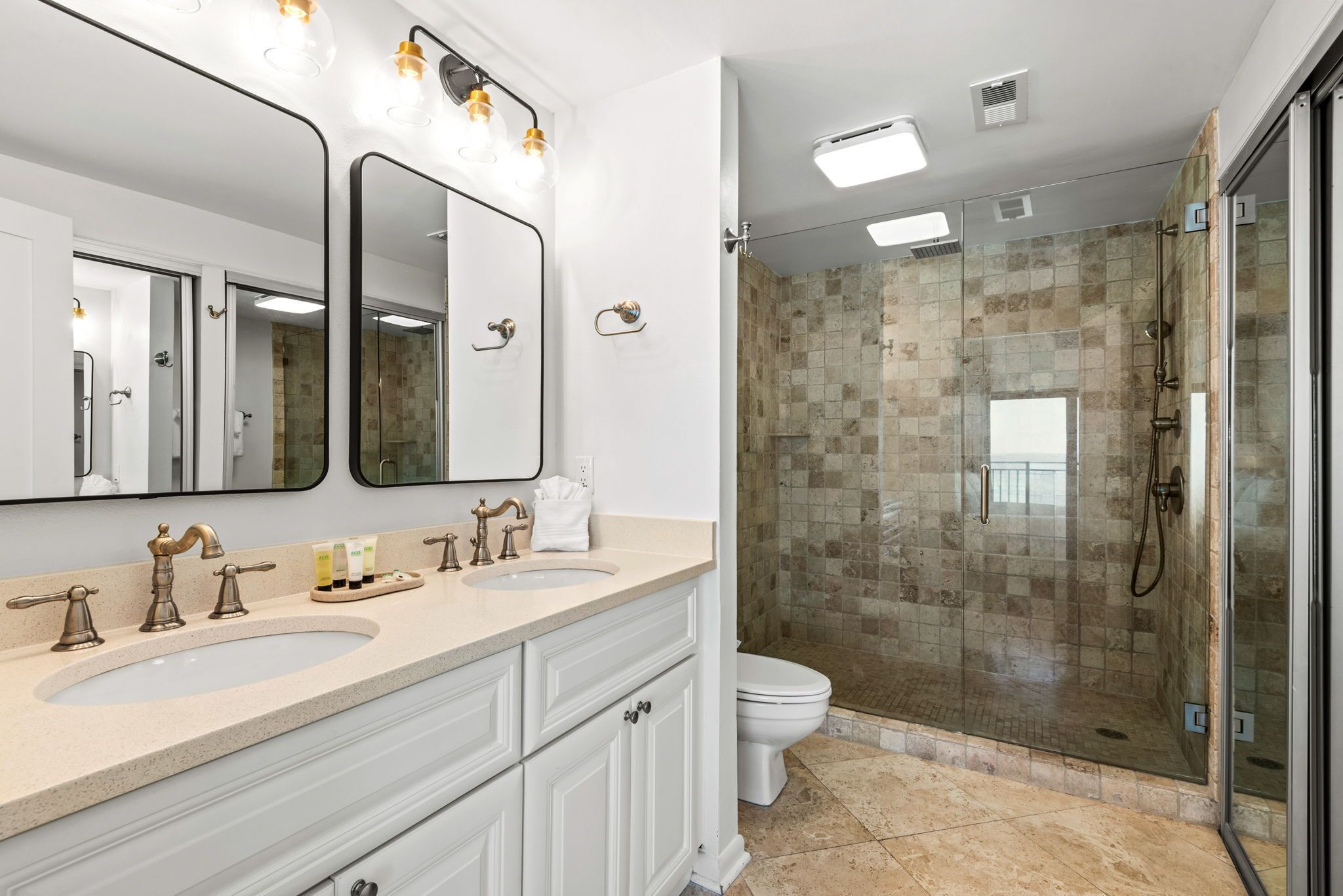 A bathroom with two sinks, a large mirror, a glass-enclosed shower, and a toilet.