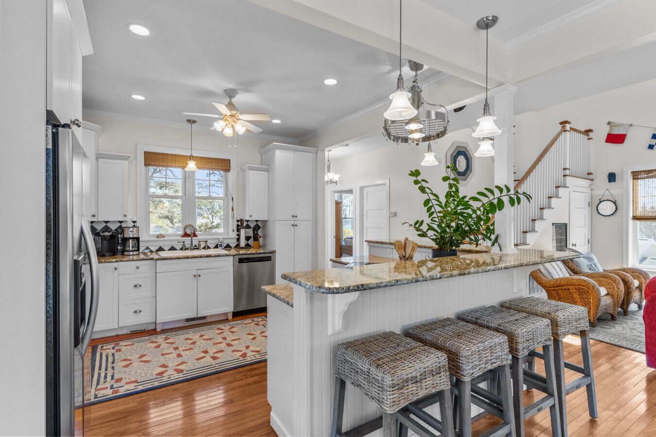 A modern kitchen with white cabinets, a central island with bar stools, and a dining area with wicker chairs.