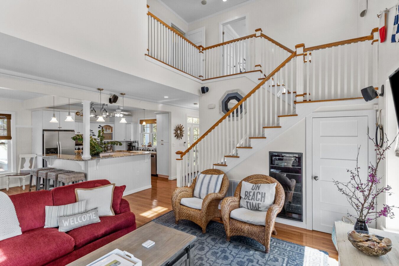 A spacious living area with a red sofa, wicker chairs, and a coffee table. A staircase with wooden railings leads to an upper level.