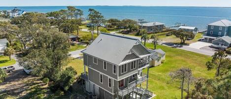 A two-story house with a balcony, surrounded by a grassy yard and trees, near a body of water.