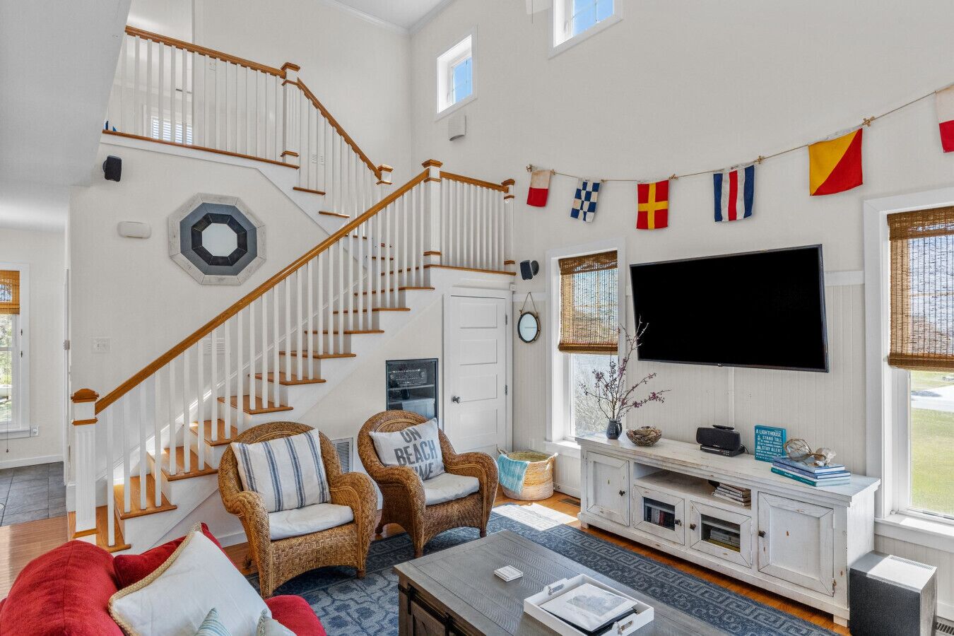 A spacious living room with a wooden staircase, wicker furniture, a flat-screen TV, and a view of the outdoors.