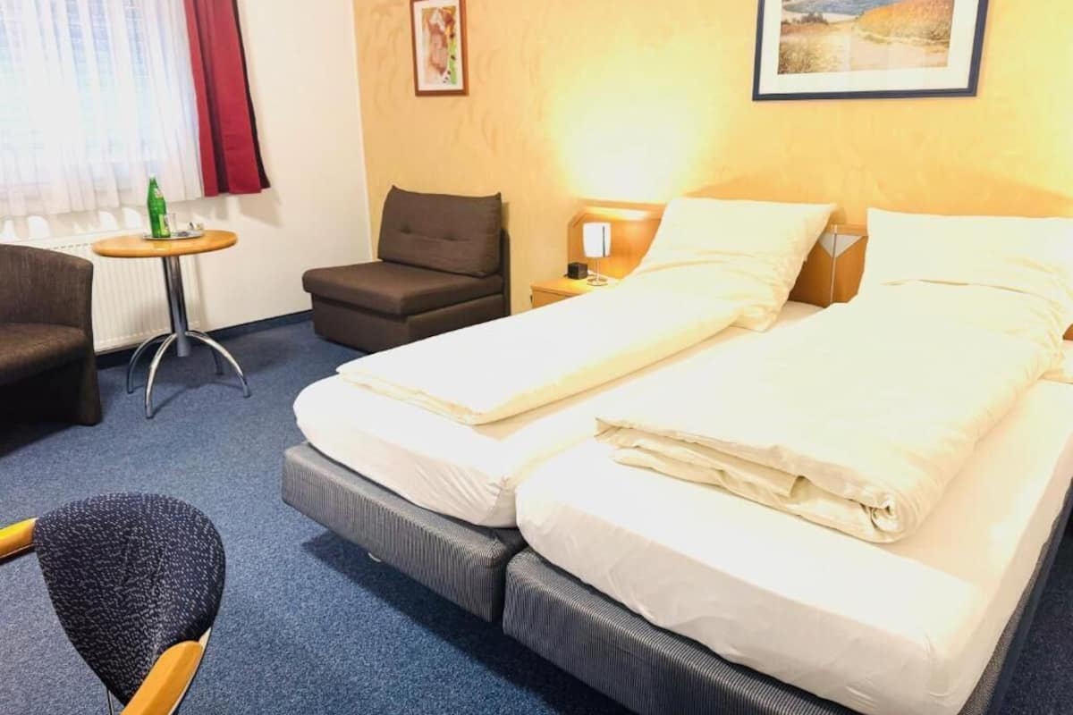 Una camera d'albergo con un letto matrimoniale, un tavolino, una sedia e una finestra con tende.