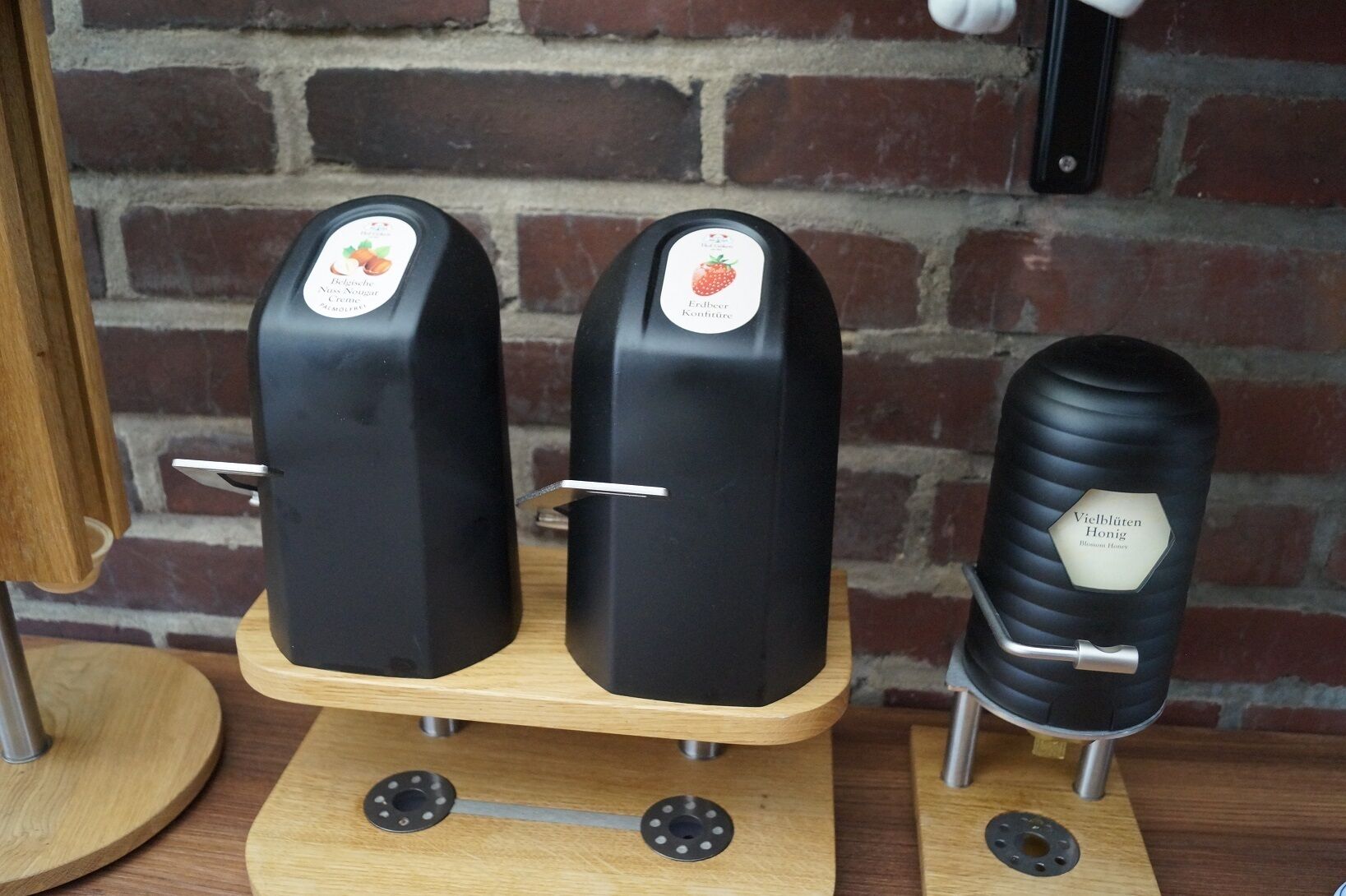 Two black vertical containers on a wooden base with metal handles, set against a brick wall.