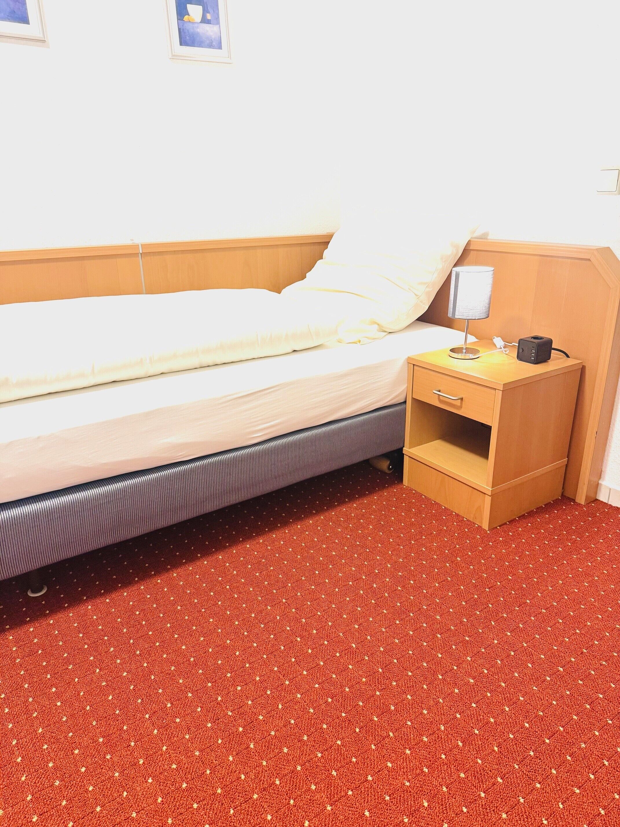 A bed with a wooden headboard, a bedside table with a lamp, and a red patterned carpet.